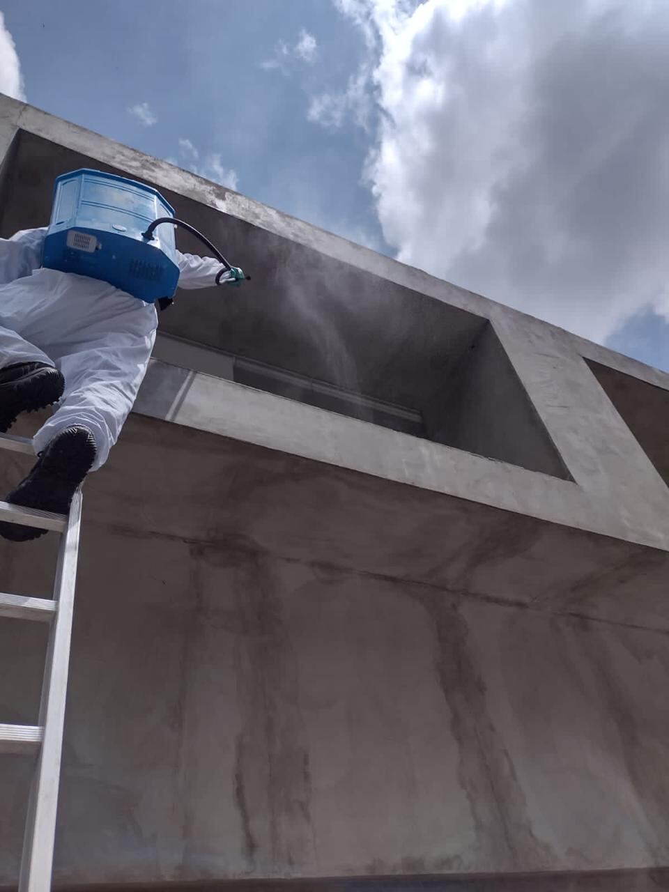 Técnico nebulizando fachada de prédio com equipamento profissional